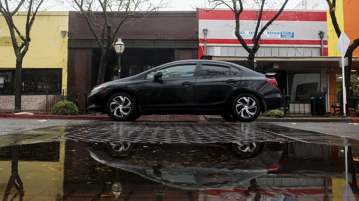 A vehicle driving along West Main Street is reflected in a puddle as rain showers move through Merced, Calif., on Wednesday, Nov. 28, 2018.