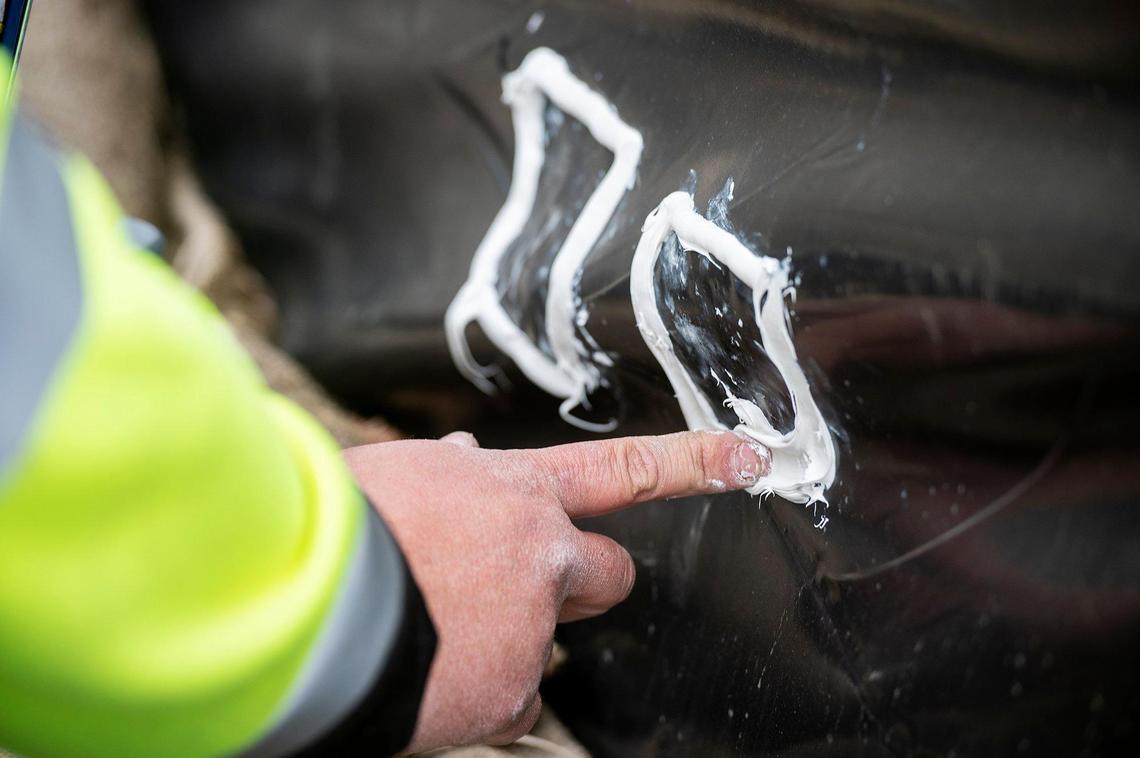 City of Merced Public Works employee Ezekiel Gurr, 29, uses caulking to patch holes and tears in plastic sheeting covering a retaining wall along West North Bear Creek drive in preparation for upcoming rainstorms in Merced, Calif., on Thursday, March 9, 2023.