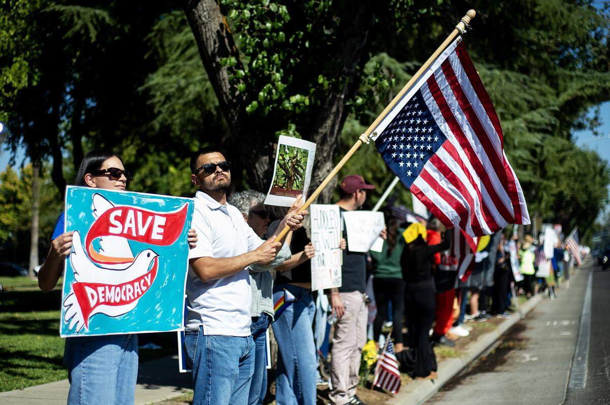 Protesters hold signs and wave flags along M Street during a “No Kings” protest in Merced, Calif., on Saturday, Oct. 18, 2025. 