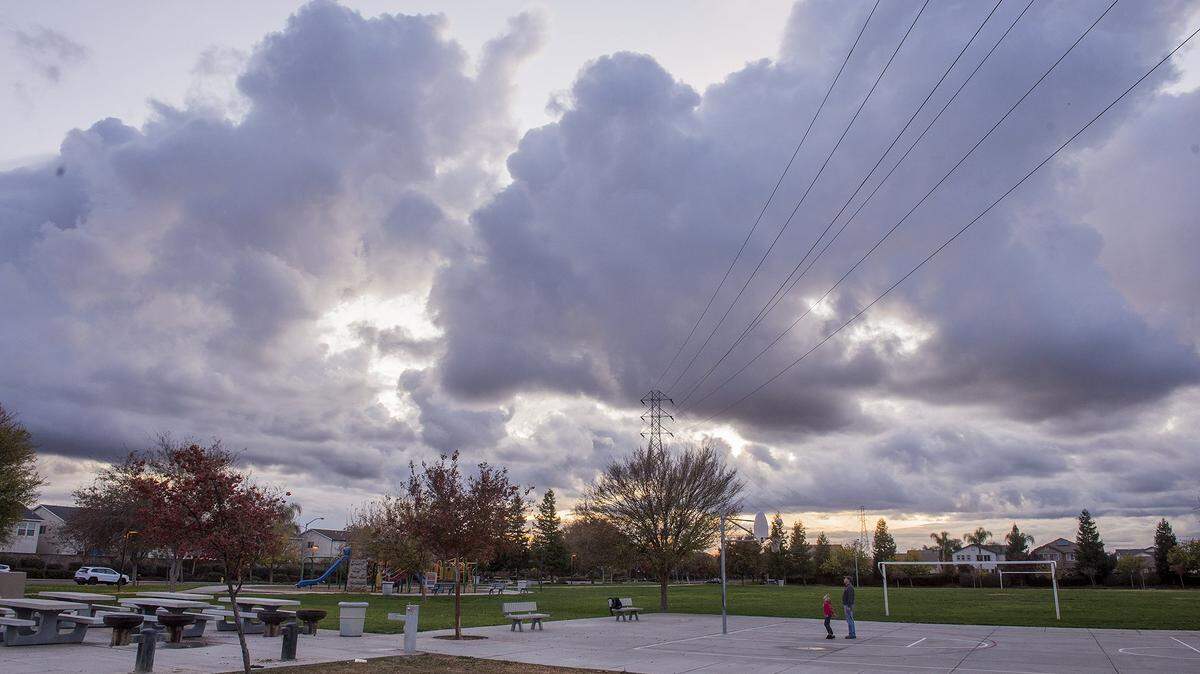 Large clouds are seen overhead as people play on the basketball court at Rudolph Joseph Merino Park in Merced, Calif., on Wednesday, Nov. 27, 2019.