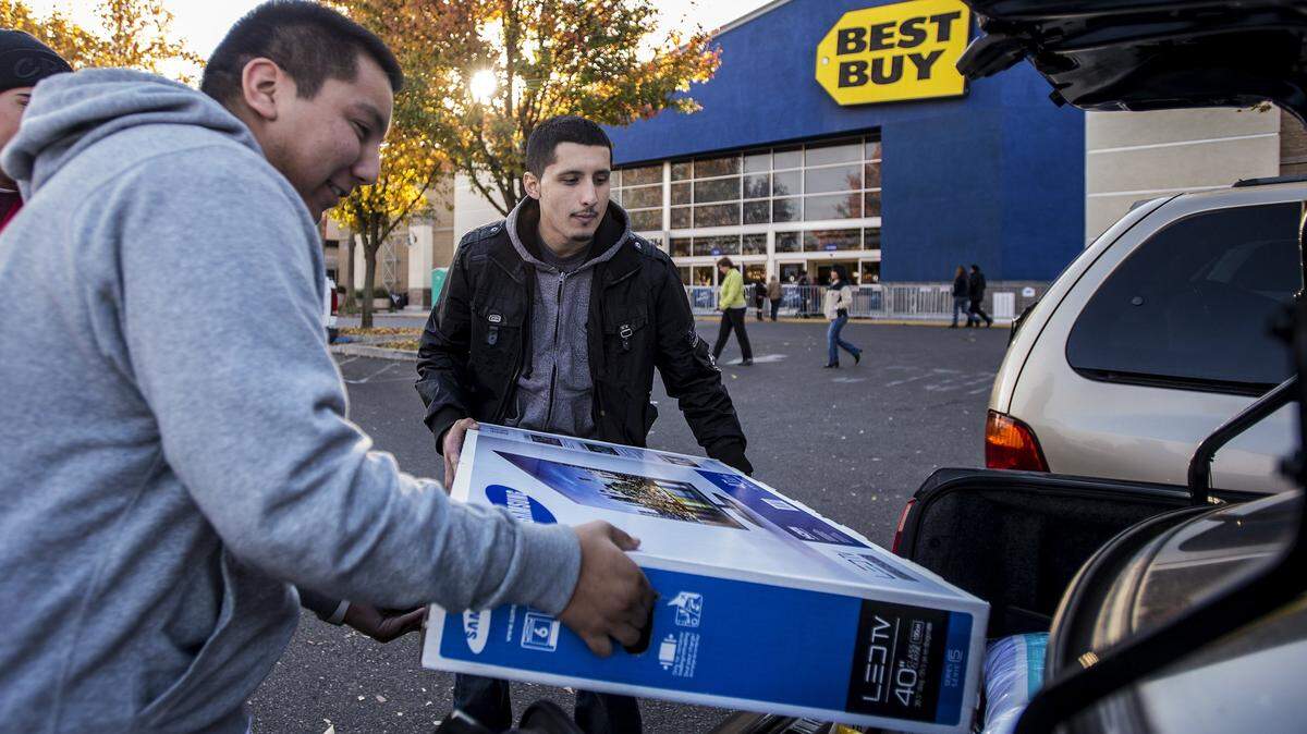 Merced residents Salvador Peralta, 21, left, and Armando Alvarez, 22, right, load a television into the trunk of the car after doing some Black Friday shopping at Best Buy in Merced, Calif., Friday, Nov. 27, 2015.