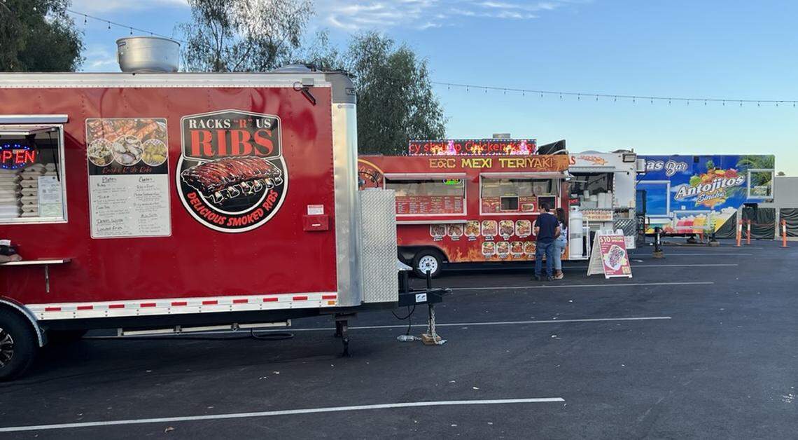 Four food trucks in angled parking spots with a few people ordering from their windows.