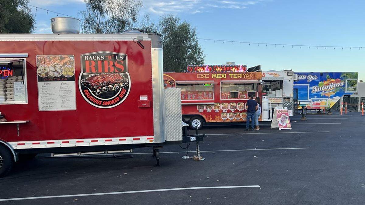 Four food trucks in angled parking spots with a few people ordering from their windows.