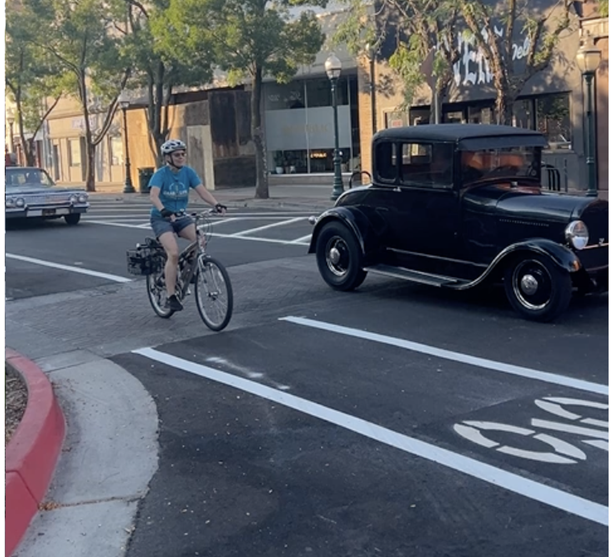 A woman on a bike rides in a bike lane beside classic cars on the road.