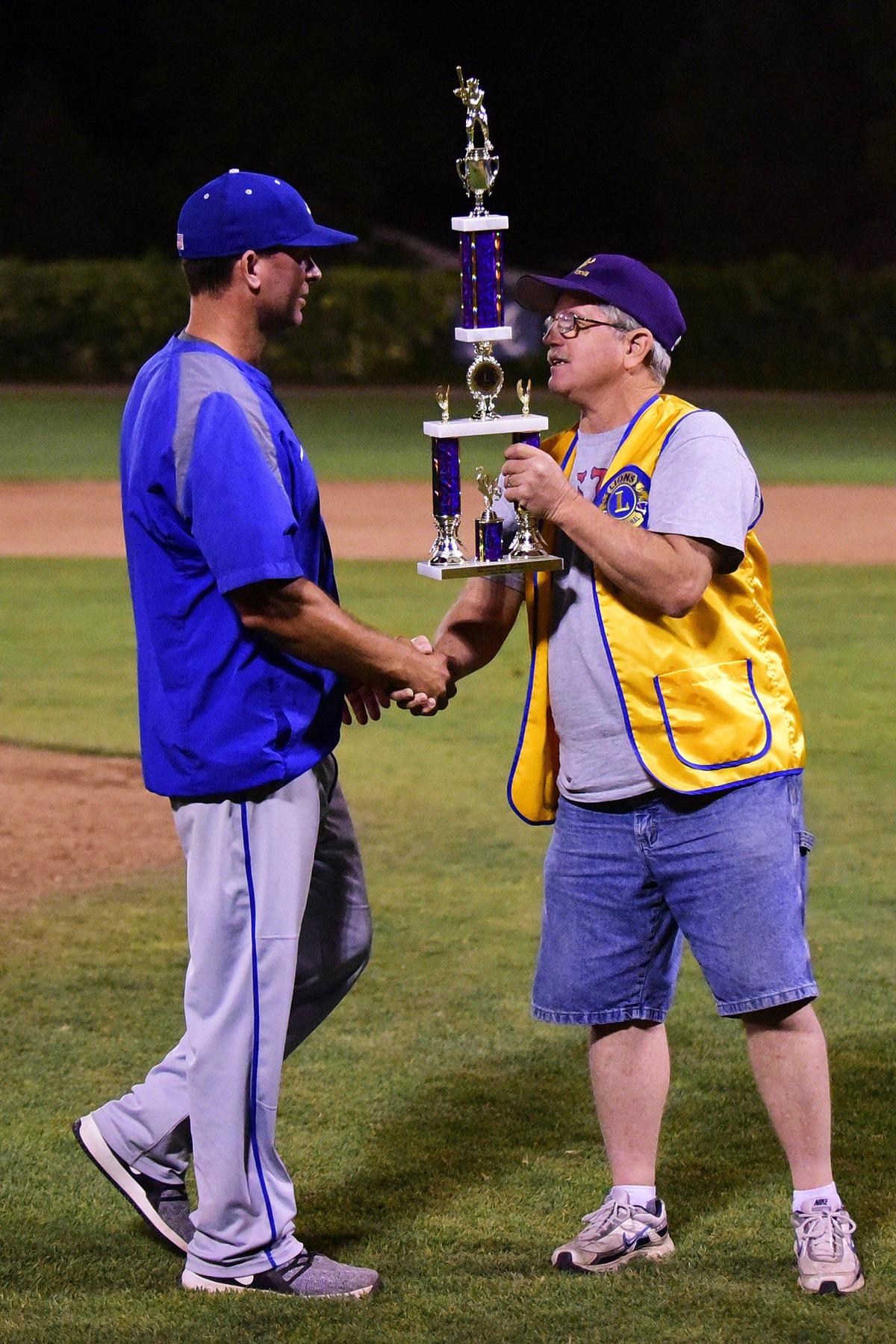 Atwater coach Jarrod Pimentel, left, is presented the championship trophy by Lions member Tom Legg, right, following the Falcons’ 8-1 win over Mountain House in the championship game of the 60th annual Fran Oneto/Atwater-Winton Lions Easter Baseball Tournament at Memorial Ballpark in Atwater, Calif., on Thursday, April 25, 2019.