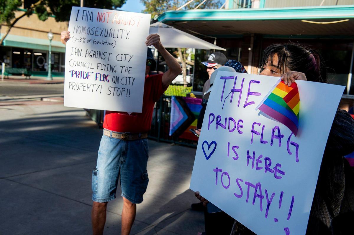 Rosy Oliveros, 21, of Oakland, right, hold a sign which reads “The Pride flag is here to stay!!” next to person with a sign stating they are against Merced City Council flying the Pride flag on city property, during the Pride Progress flag raising ceremony at Bob Hart Square in Merced, Calif., on Wednesday, June 1, 2022. The Merced City Council approved the addition of the Pride flag to the regular flag calendar, meaning the flag will fly over Bob Hart Square annually during the month of June.
