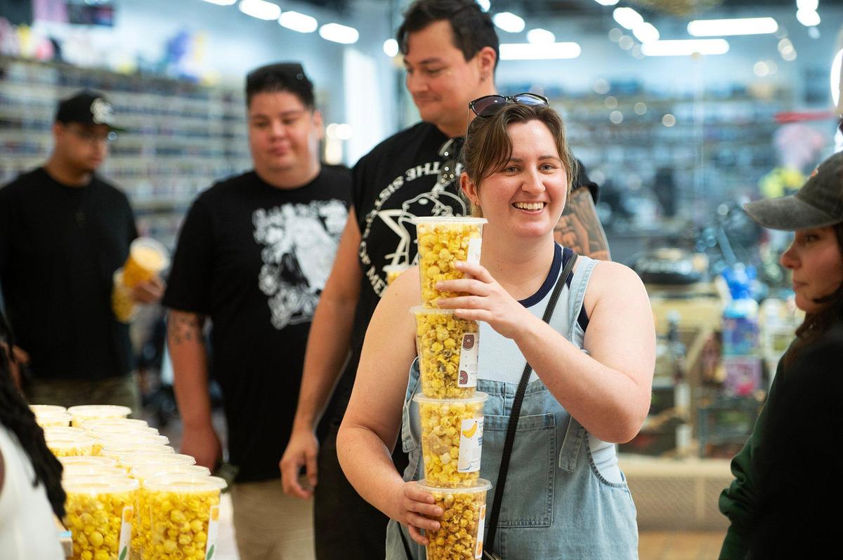 Ashley Fazzari, 27, a local zookeeper, waits in line to pay for the containers of popcorn she chose during the grand opening of Dom’s Bomb Gourmet Popcorn inside the Marketplace at Merced in Merced, Calif., on Thursday, May 1, 2025. The kiosk offers unique gourmet popcorn flavors created by Merced resident Dominique Pruitt.
