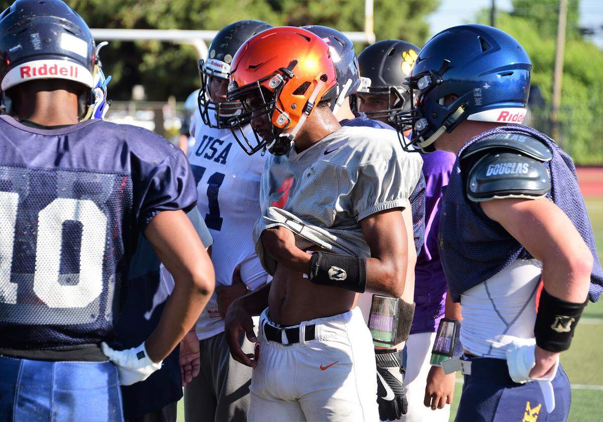 Former Merced High receiver Xavier Stewart (orange helmet) and other South players look on in a huddle during a practice for the North/South Rotary Bob Green Football Classic at Atwater High in Tuesday, June 18, 2019.