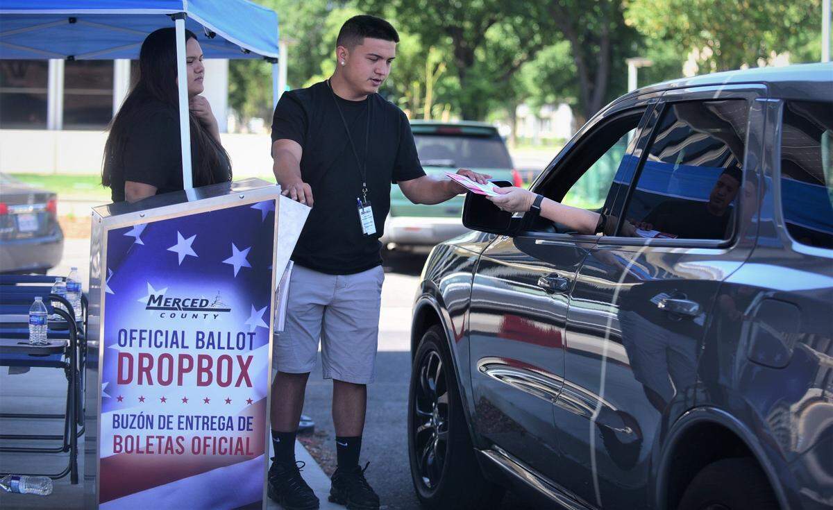 Election workers Alex Gonzales and Melina Gonzales help voters submit their ballots at the drive-through dropoff box in front of the Merced County Administration Building on Tuesday, June 7, 2022.
