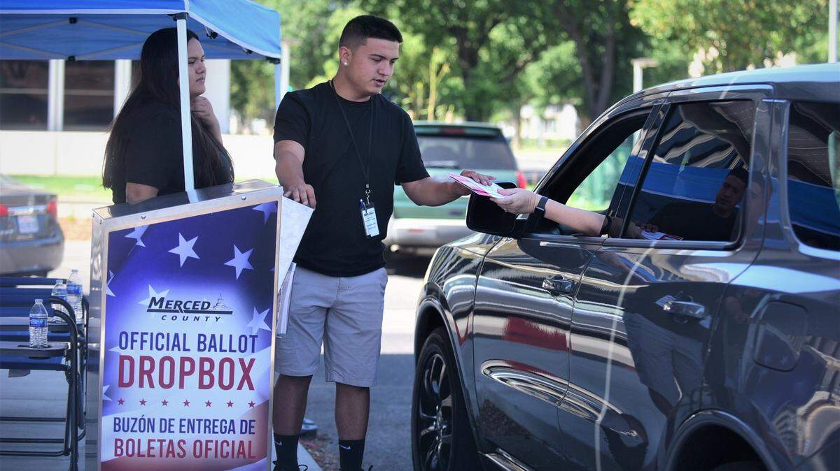 Election workers Alex Gonzales and Melina Gonzales help voters submit their ballots at the drive-through dropoff box in front of the Merced County Administration Building on Tuesday, June 7, 2022.