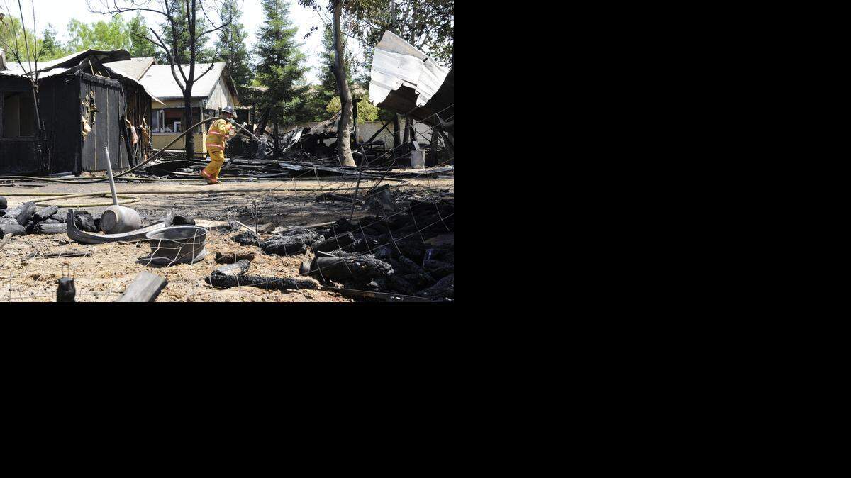 A fireman pulls a hose through property that was destroyed by a fire that broke out, displacing 15 residents of four houses and killing several animals at Kibby Road near Highway 140 on Wednesday, May 28, 2014, in Merced.
