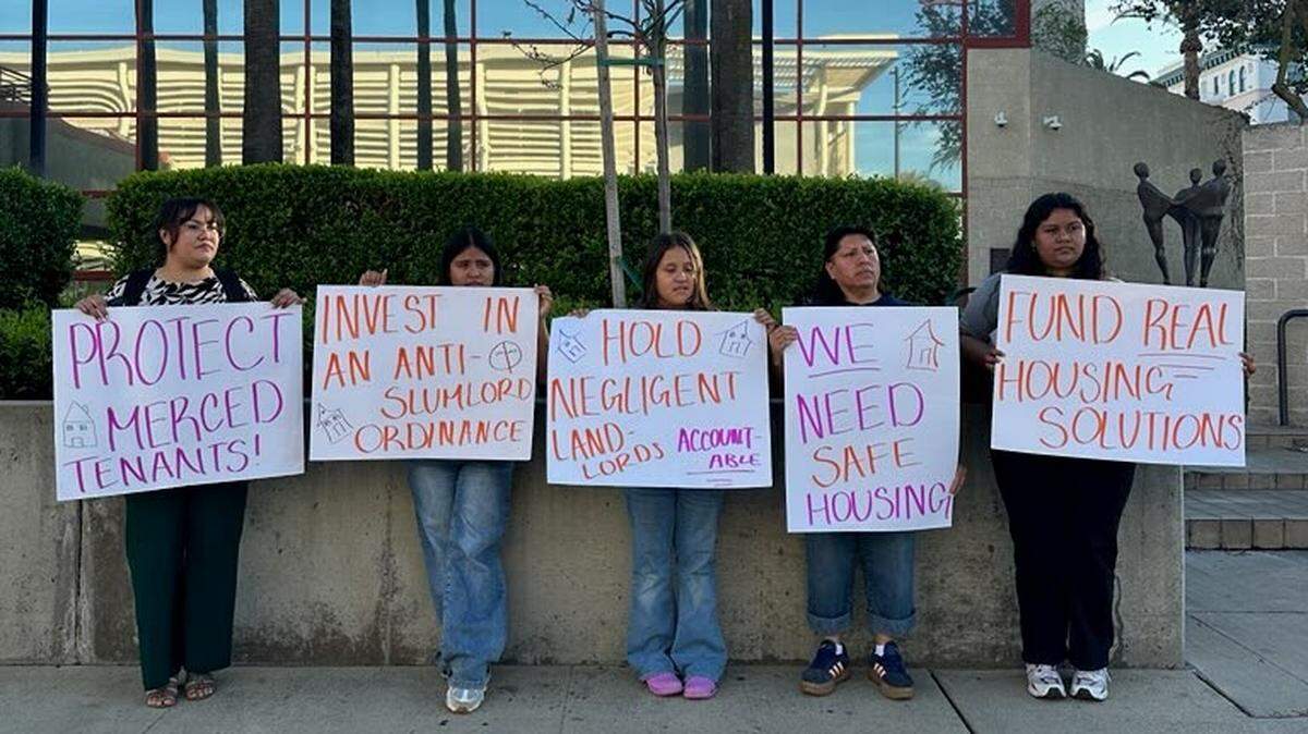 Five young women stand outside the city center holding signs advocating for renter protection.