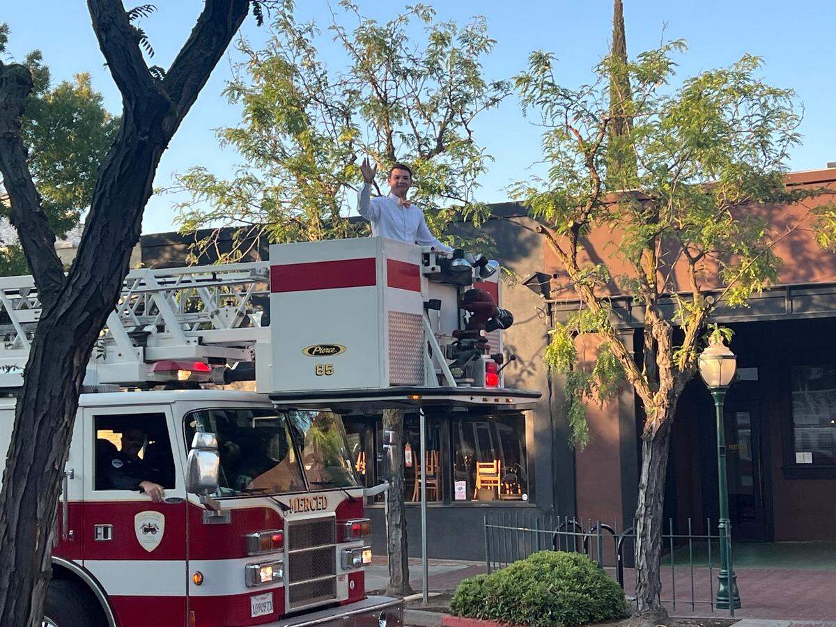 A man raises his hand to wave from the basket of a fire department ladder truck.