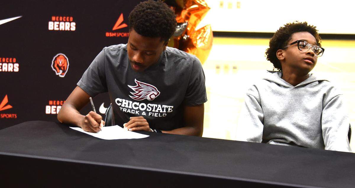 Merced High School senior Donovan Marshall (left) signs his national letter of intent to attend Chico State during a ceremony while his younger brother Brayden is seated next to him on Tuesday, May 28, 2024.