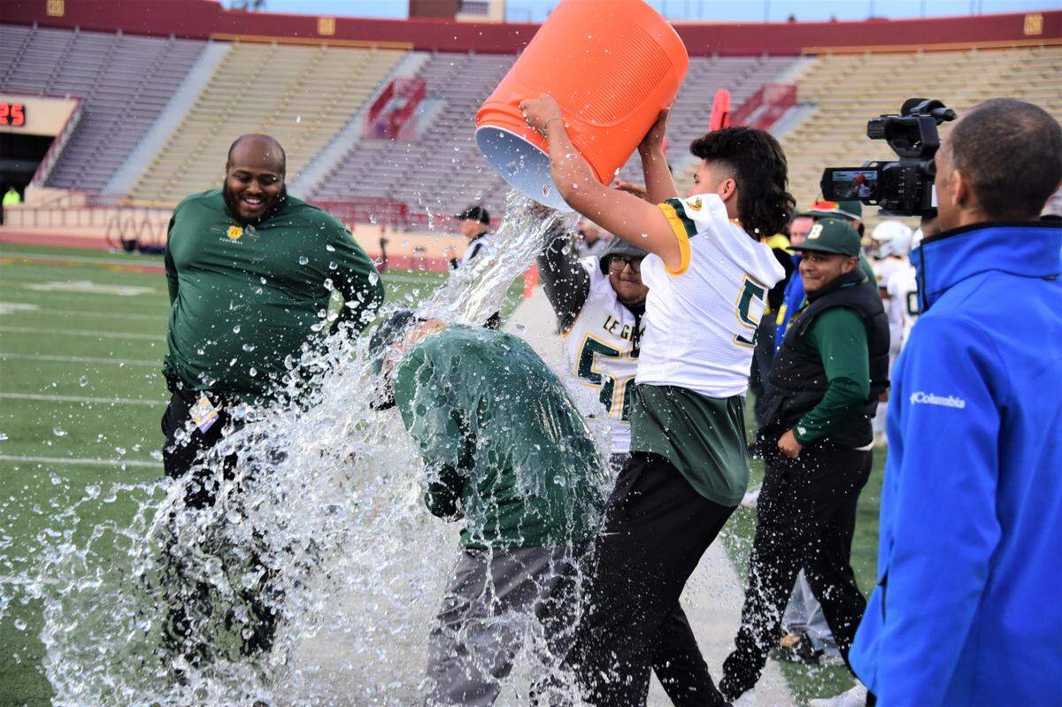 Le Grand High senior Aaron Martinez Jr. dumps the Gatorade bucket over his father and Bulldogs head coach Aaron Martinez Sr. during Le Grand’s 35-12 win over Woodland Christian in the Sac-Joaquin Section Division VII championship game at Hughes Stadium in Sacramento, Calif.