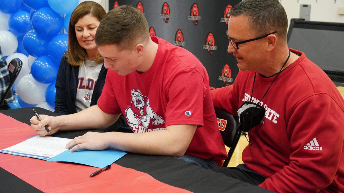 Merced High senior Seth Scheidt signs his national letter of intent to play football at Fresno State as his mother Sandra Scheidt and father Rob Scheidt look on during a signing ceremony at Merced High on Wednesday, Feb. 2, 2022.