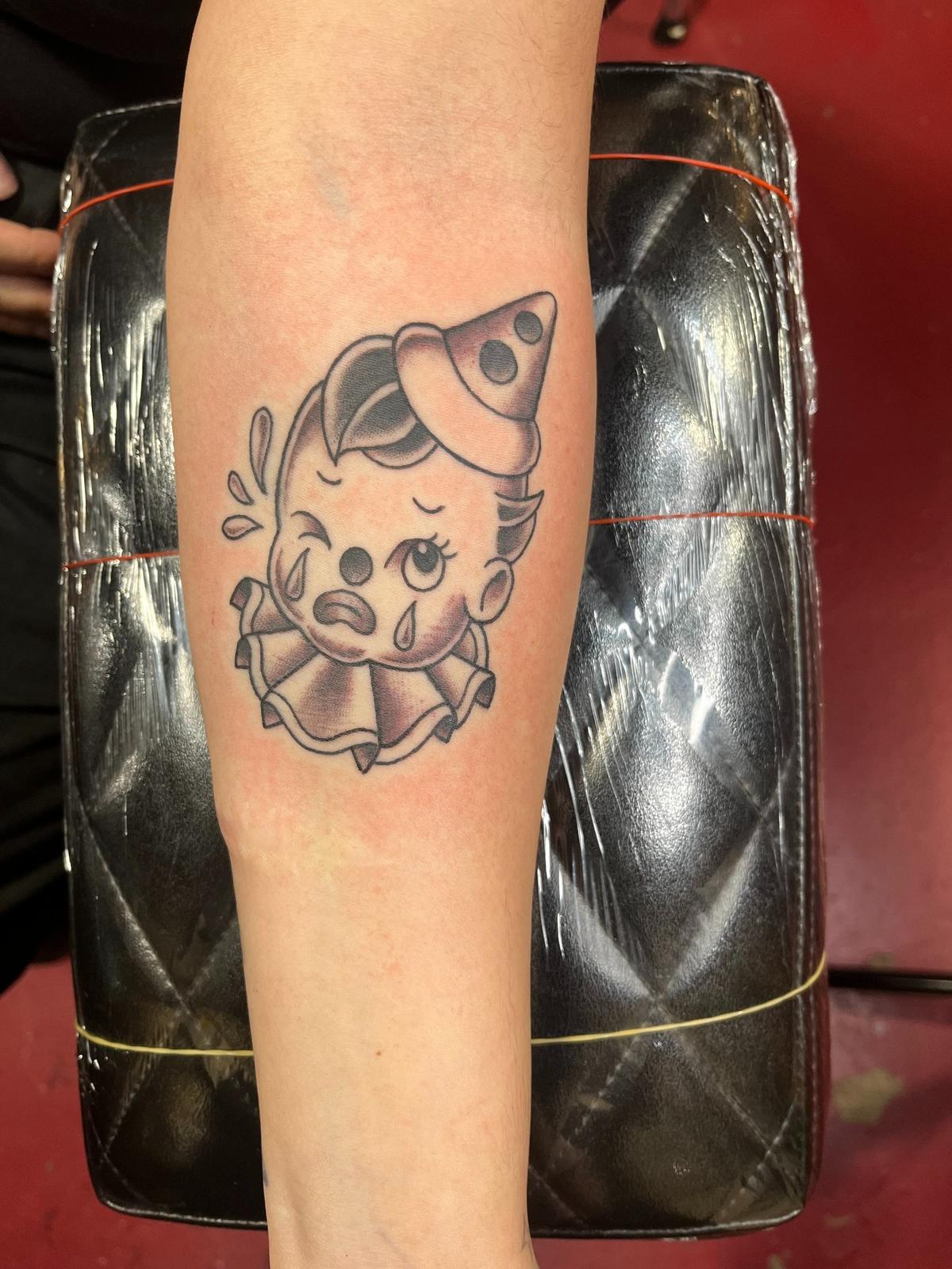 Pre-designed tattoo of a crying and winking cartoon clown on a customer’s forearm by Main Street Tattoo and Body Piercing artist, “Little” Johnny Tharp. His daughter, Paulette Busbea, owns the parlor. Courtesy of “Little” Johnny Tharp.