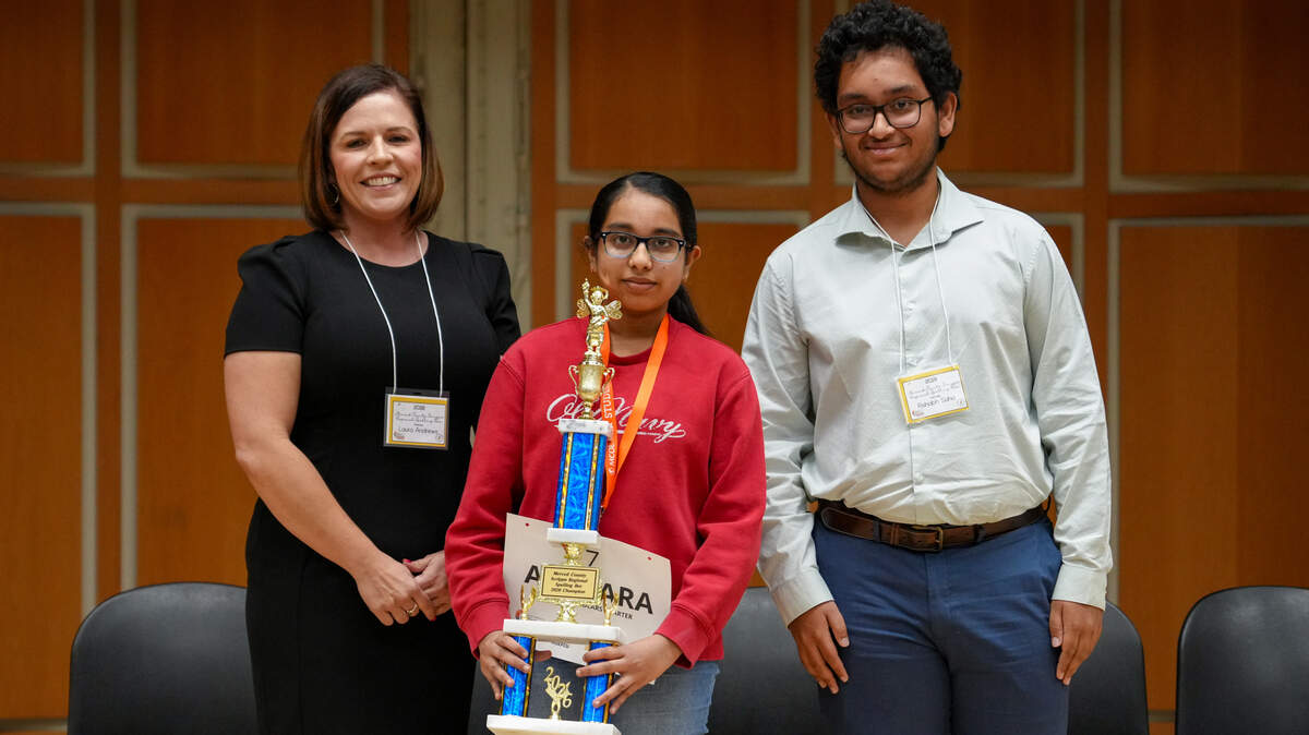 Akshara Thummala, winner of the Scripps Regional Spelling Bee, holds her trophy and stands with the competition judges.