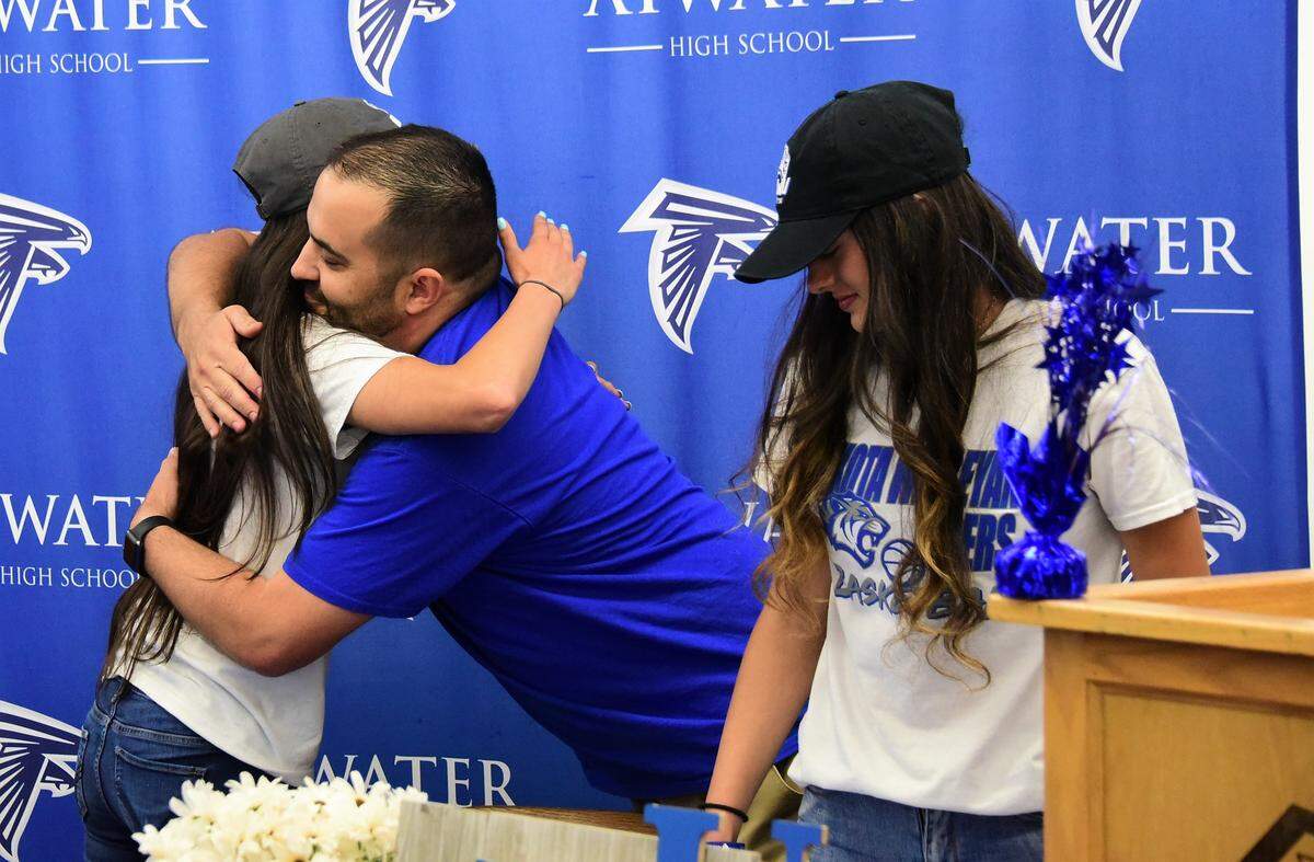 Atwater High senior Lexi Valencia (left) is congratulated by Atwater activities director Nathan Braga as Kelsey Valencia looks on. The Valencia twin sisters signed their national letter of intent to accept a basketball scholarship to Dakota Wesleyan University on Tuesday, April 30, 2019 at Atwater High.