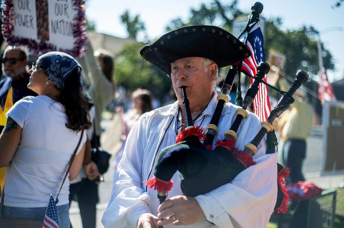 Ken Mackie, 70, of Merced, walks along M Street playing the bagpipes with a Betsy Ross flag during a “No Kings” protest in Merced, Calif., on Saturday, Oct. 18, 2025. 
