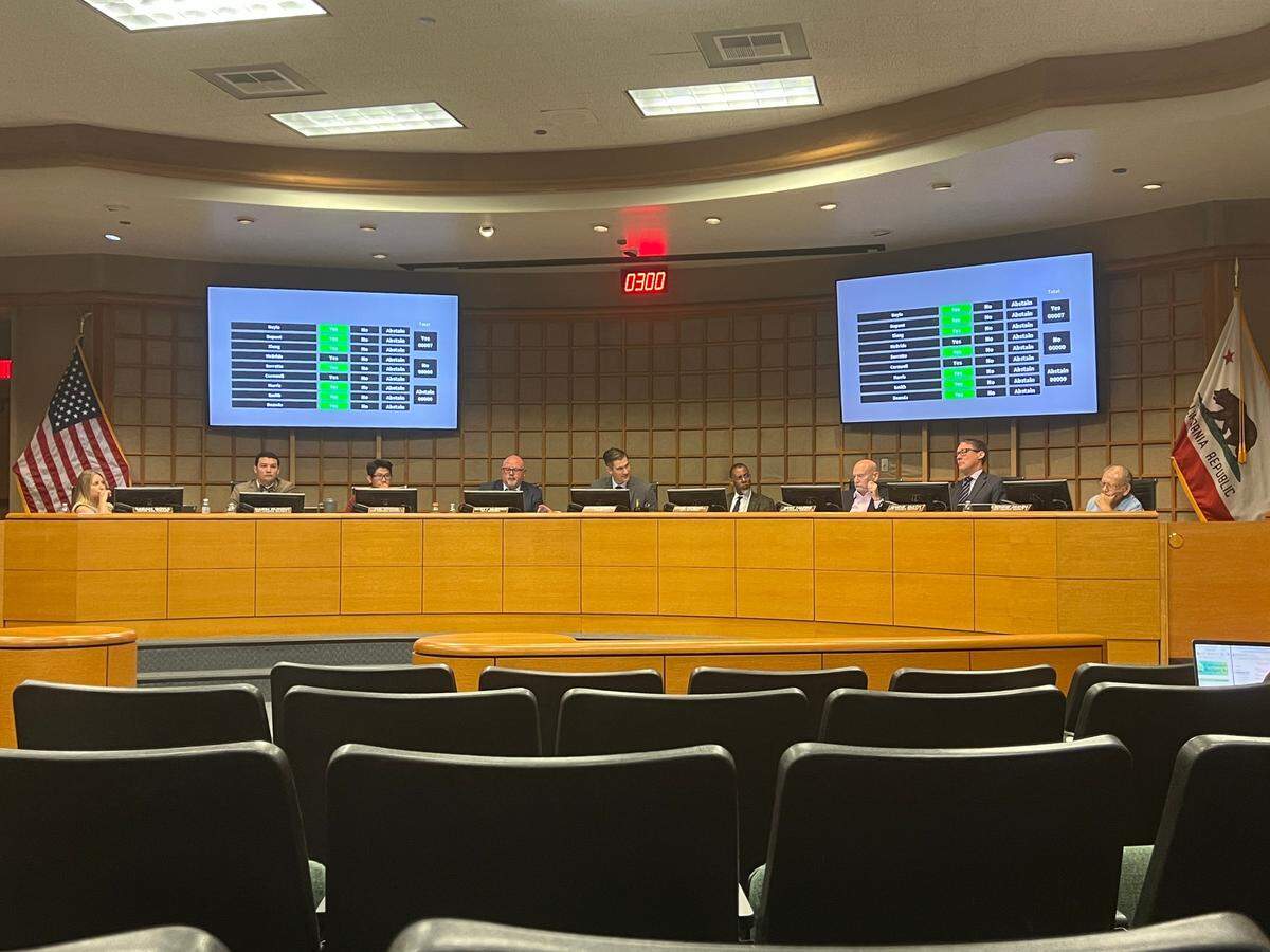 Nine people sit behind a raised curved dais