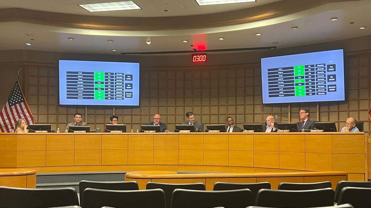 Nine people sit behind a raised curved dais