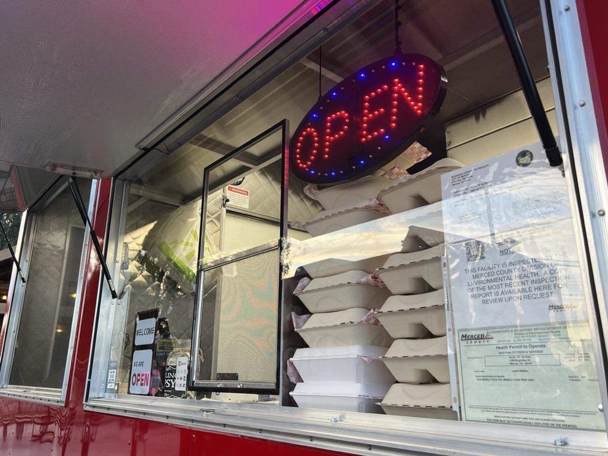 The order window of a food truck with a business license and health inspection taped to the window on the inside. 