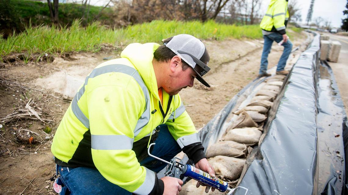 City of Merced Public Works employee Ezekiel Gurr, 29, uses caulking to patch holes and tears in plastic sheeting covering a retaining wall along West North Bear Creek drive in preparation for upcoming rainstorms in Merced, Calif., on Thursday, March 9, 2023.