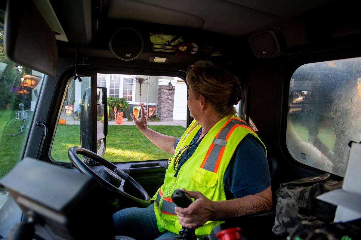 Merced Refuse Equipment Operator Kristie Light, 56, waves to children at a daycare along her route while collecting refuse in Merced Calif. on Thursday, Oct. 24, 2024. According to Light who previously drove commercial trucks across parts of the country and would routinely be gone for 70-80 hours a week, her current job with the city allows her to spend more time at home. “It’s nice to go to work and like your job,” said Light.