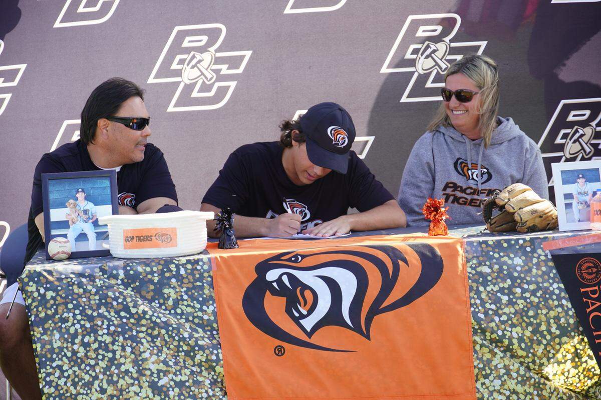 Buhach Colony High School senior Cooper Lanz signs his national letter of intent to accept a baseball scholarship to the University of the Pacific as his parents Robert and Gena Lanz look on during a ceremony on the Buhach Colony baseball field on Monday, May, 2, 2022.