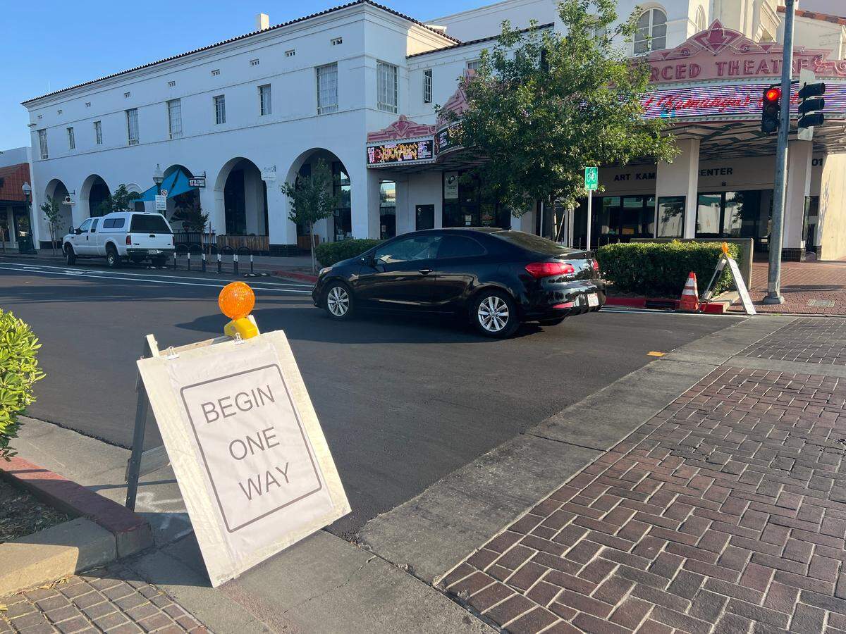 A white easel sign says "Begin One Way" at the intersection of a street.