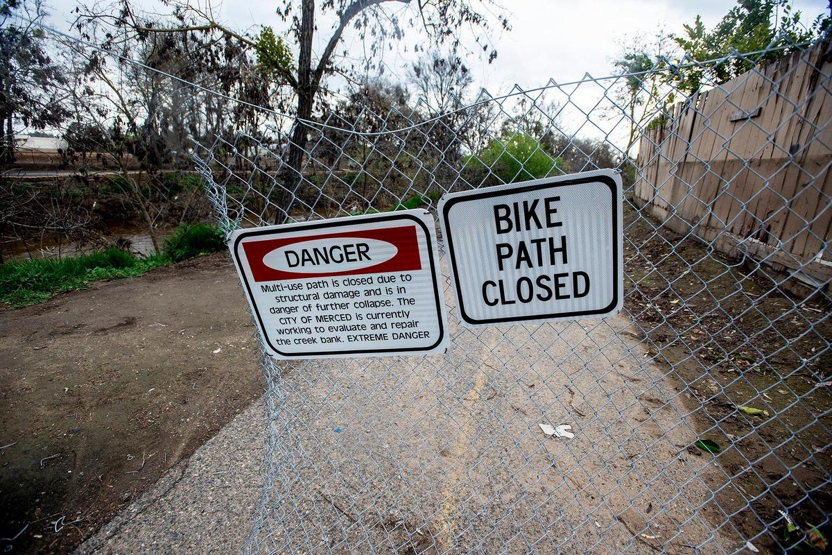Signs warn pedestrians of a dangerous section of bike path along Bear Creek near West 25th Street in Merced, Calif., on Tuesday, March 14, 2023.