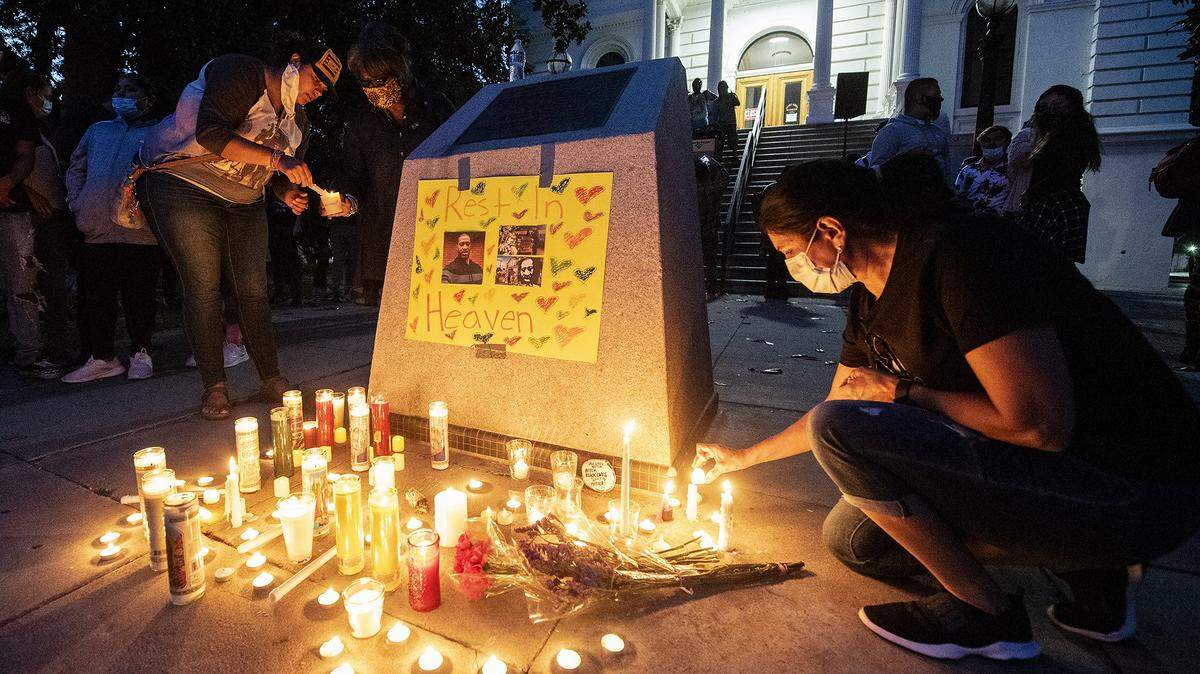 People place candles near images of George Floyd during a candlelight vigil in his memory and others who lost their lives to police brutality at the Merced County Courthouse Museum in Merced, Calif., on Friday, June 5, 2020.
