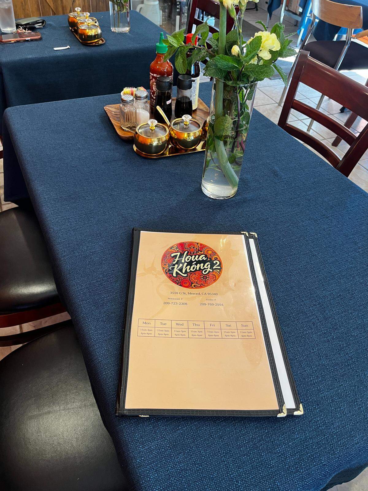 Houa Khong 2 Menu on a blue tablecloth with condiments and flowers behind it.