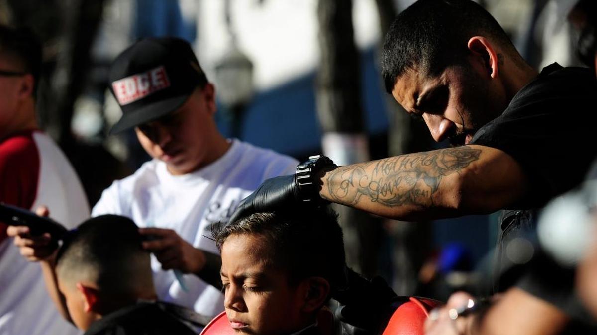 At right, Chris Castaneda, 27, a barber at The Shop, cuts the hair of George Zayas, 7, of Merced during the Cheerful Giving event Saturday in downtown Merced.