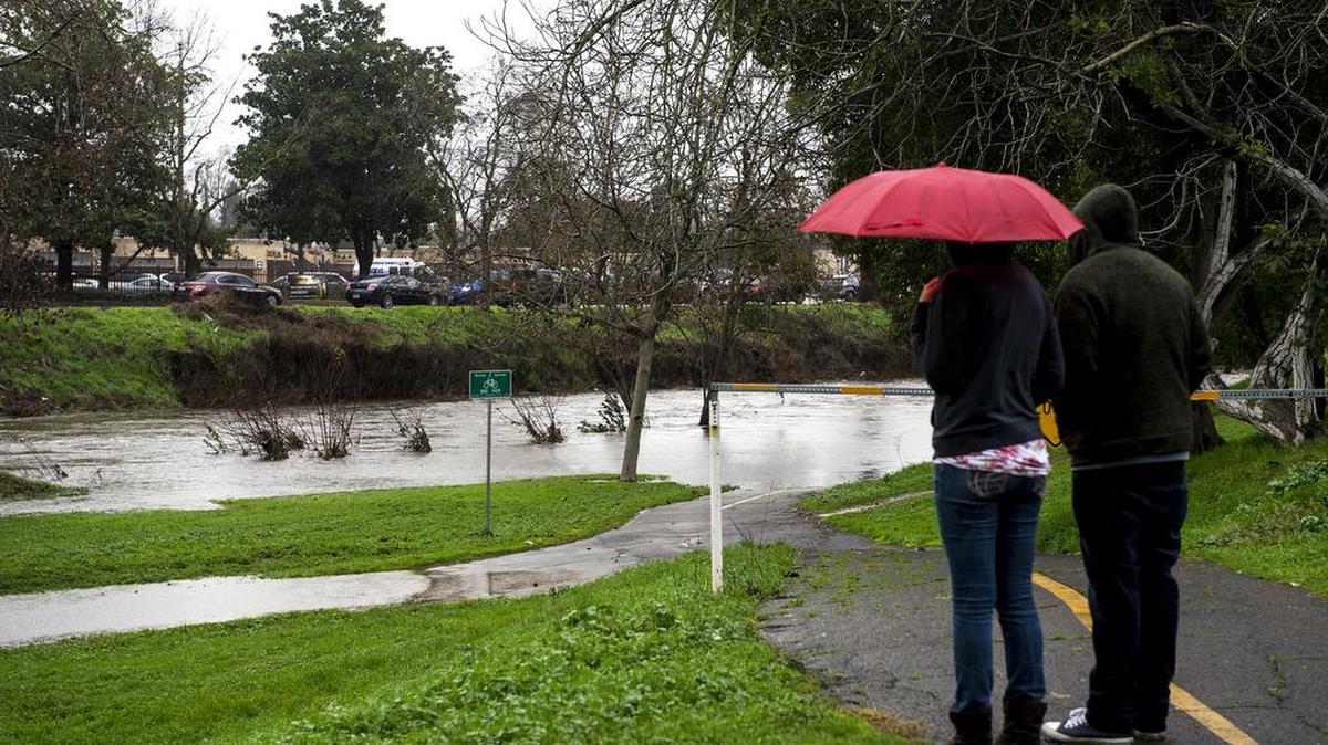 Samantha Kudulis, 24, left, and Brendan Simpson, 26, right, both of Merced, look on as Bear Creek floods part of the Michael O. Sullivan Bike Path in Merced on Tuesday.