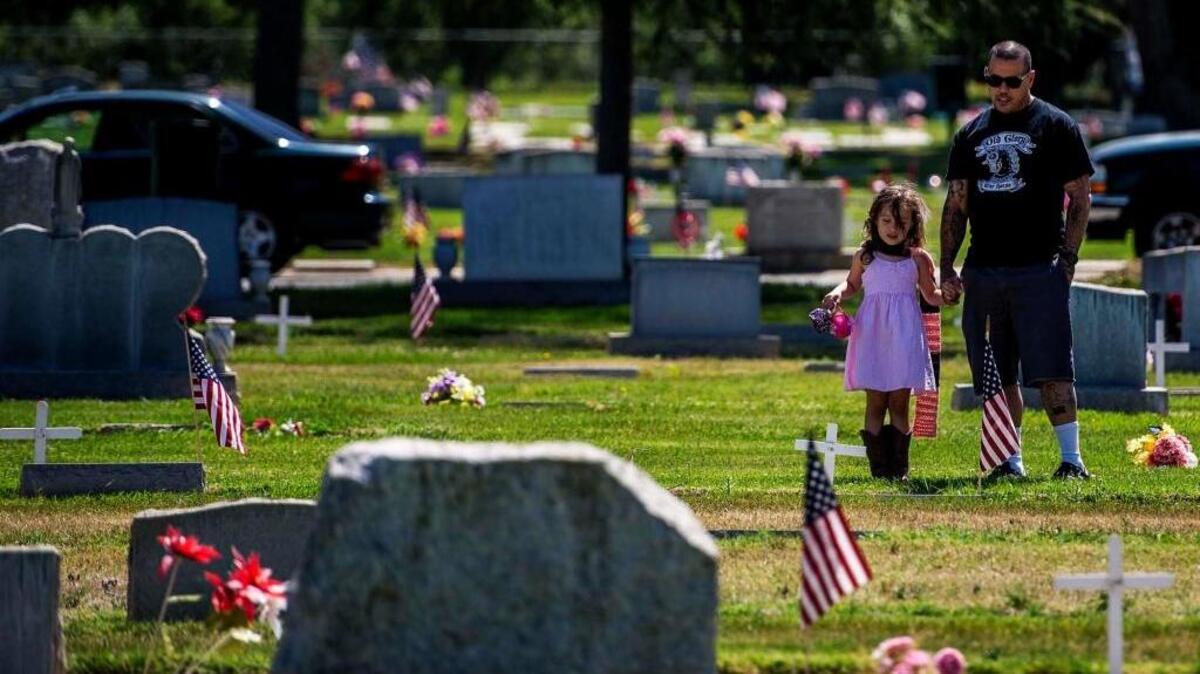 Sean Garcia of Atwater shows his daughter, Molly, the graves of family members who served in the armed forces during a Memorial Day ceremony at Winton Cemetery in 2015. Many government offices and services are affected by the national holiday, which falls this year on Monday.