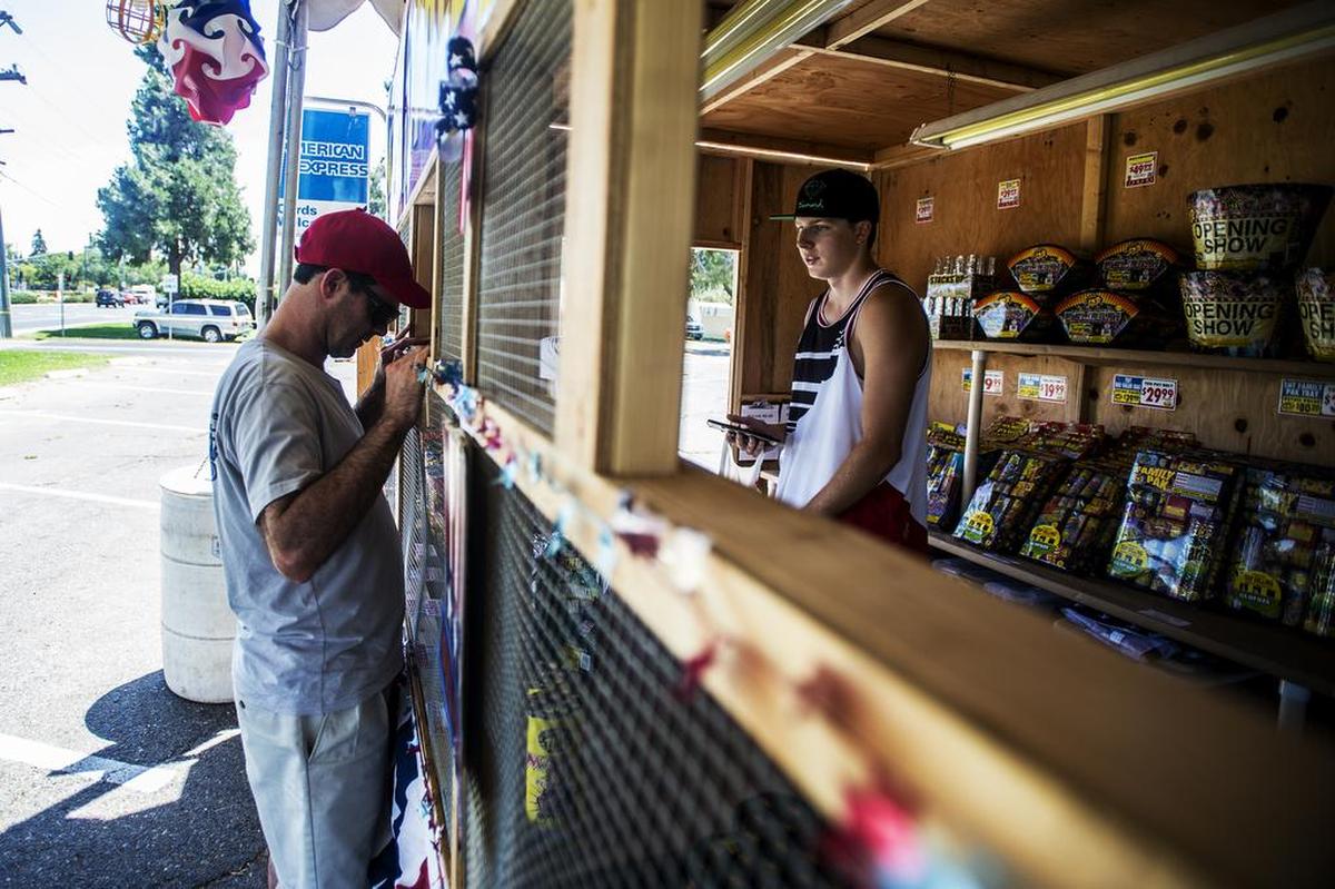 Michael Dockery, 19, of Merced, assists a customer in purchasing fireworks at the TNT fireworks stand near G Street and Olive Avenue in Merced on Tuesday.