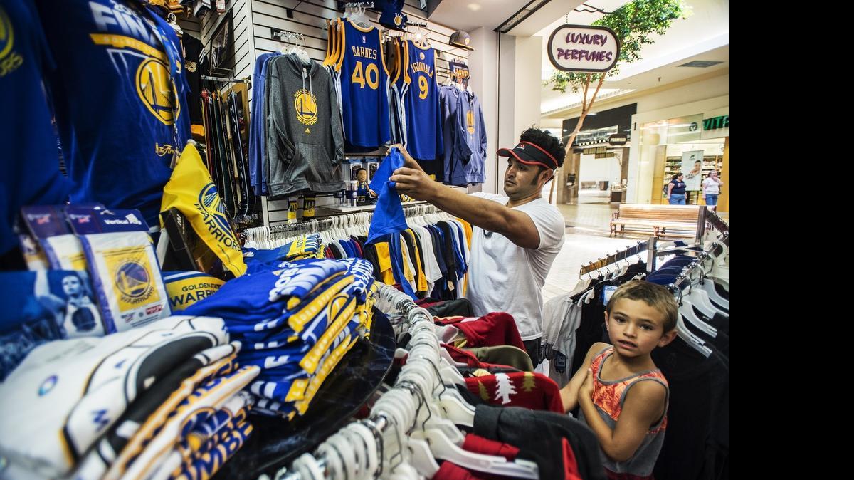 
Merced resident Cisco Jimenez and son Max, 6, look at Golden State Warriors apparel at All American Sports Fan in the Merced Mall on Wednesday. According to district manager Don Smith, the store has been bombarded with customers seeking Golden State Warriors apparel after the team won its first NBA Championship since 1975 by defeating the Cleveland Cavaliers 105-97 in Game 6 on Tuesday night.
