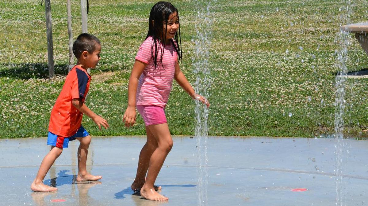 In this 2016 photo, 7-year-old Kimberly Santana and 4-year-old brother Jonathan Santana keep cool by jumping on the splash pad at McNamara Community Park in Merced.