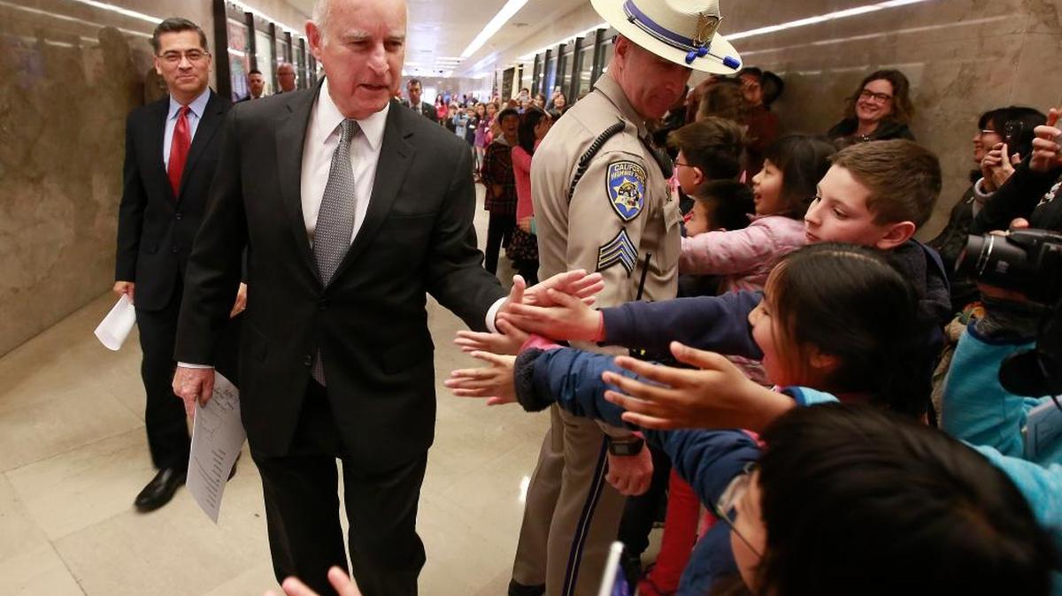 California Gov. Jerry Brown is greeted by children as he walks through the Capitol with California Attorney General Xavier Becerra, left, to hold a news conference in response to remarks made U.S. Attorney General Jeff Sessions, Wednesday, March 7, 2018, in Sacramento, Calif. (AP Photo/Rich Pedroncelli)