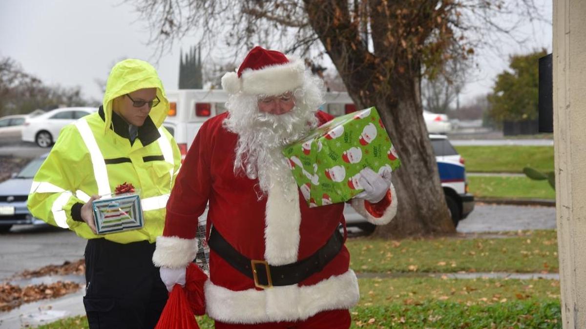 Santa Claus and Riggs Ambulance Service employees bring presents to a Merced family on Friday. Riggs presented gifts to seven families throughout the county this year.