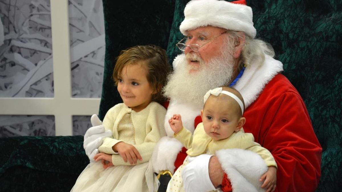 From left, 3-year-old Bella Holmes and 7-month-old Maddie Holmes sit on Santa Claus’ lap for a photo Saturday at the Merced Mall. Bella asked Santa for a stuffed bear for Christmas.