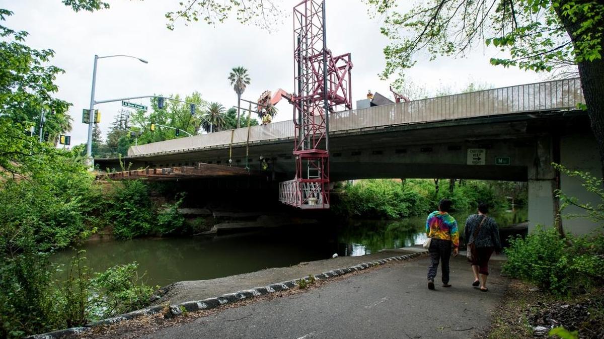 Pedestrians walk beneath M Street as Viking Construction Co. workers prepare the M Street bridge for rehabilitation work in Merced, Calif., on Tuesday, April 18, 2017. Work will be done to rehabilitate the bridge structure, the roadway and the creek channel.