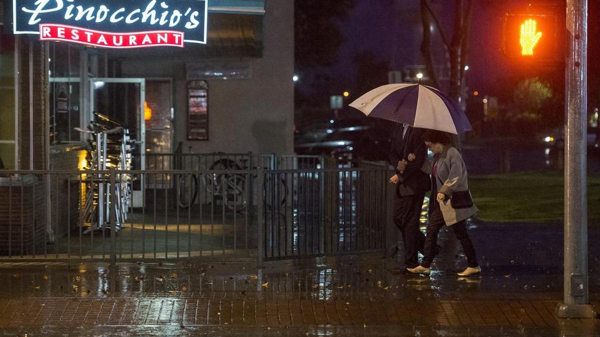 Pedestrians walk along Main Street on a rainy Saturday night in Merced on March 5, 2016.