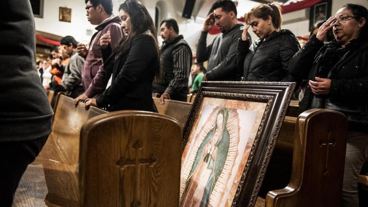 A painting of the Virgin of Guadalupe sits next to churchgoers as they make the sign of the cross during Mass during Virgin of Guadalupe festivities at Sacred Heart Catholic Church in Merced on Wednesday. The celebration lasts for nine days leading up to Dec. 12, the Day of Our Lady of Guadalupe.