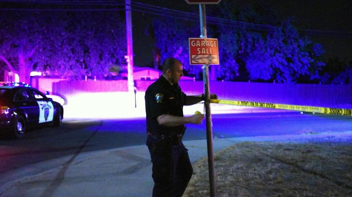 
A police officer ties crime-scene tape to a stop sign at the intersection of Eighth and W streets late Saturday in Merced. One man was shot while driving a vehicle, investigators said.
