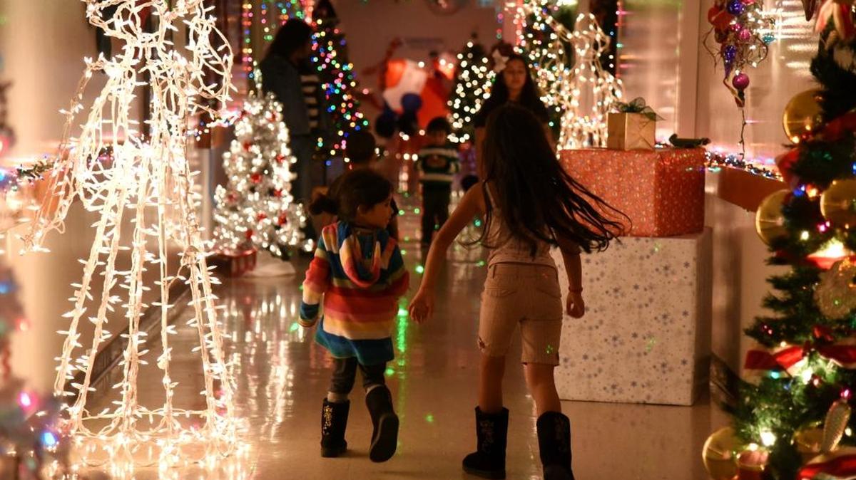 Children walk down a decorated hall at Castle Family Health Centers in Atwater on Monday. Some families won trees in a lottery.