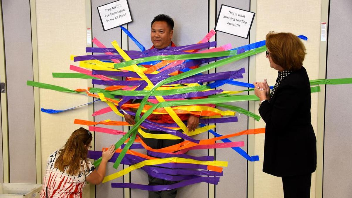 Rick Her, principal at Joe Stefani School, was taped to the cafeteria wall Tuesday, Oct. 20, 2015, by students who earned the most points by reading the most words. Taping the principal to the wall served as incentive for students to read. The next reading incentive is to have the school’s learning director, Juanita Pedrozo, kiss a pig.