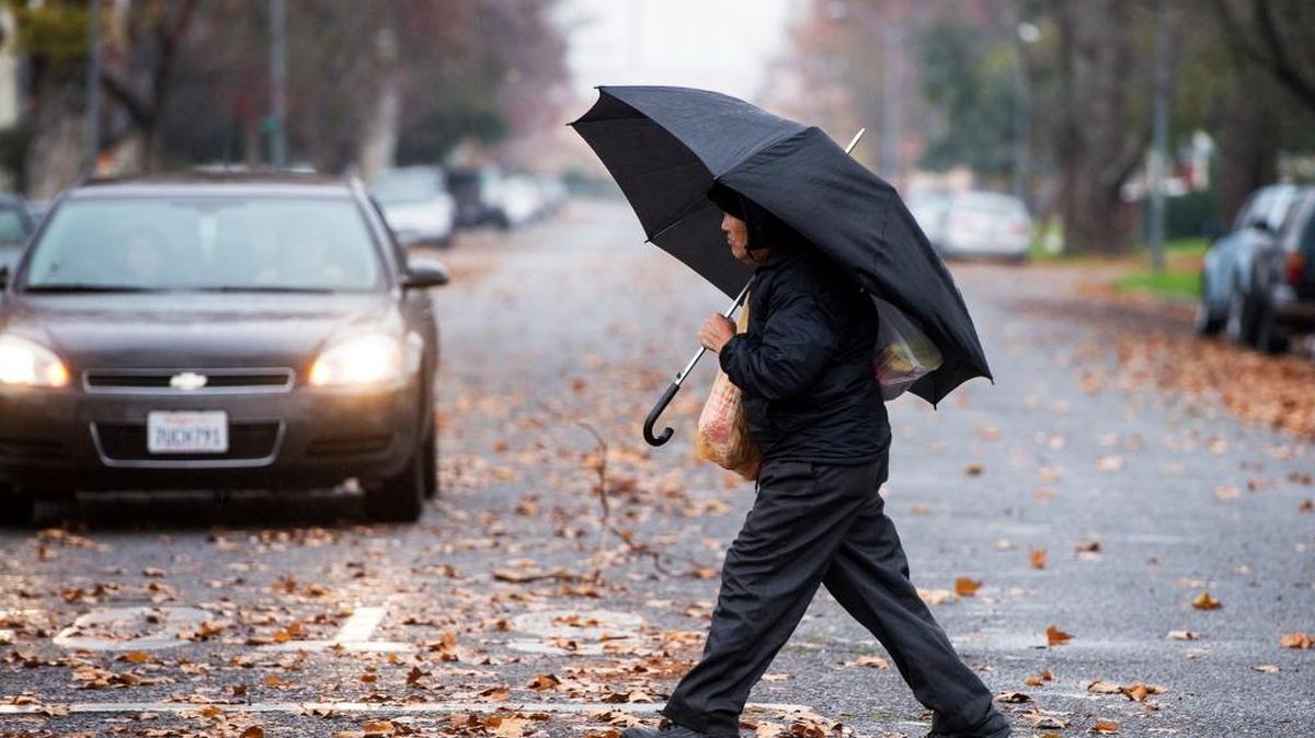 A man carries groceries across West 19th Street while taking shelter from the rain under his umbrella during a rainy day in Merced, Calif., on Friday, Dec. 23, 2016.